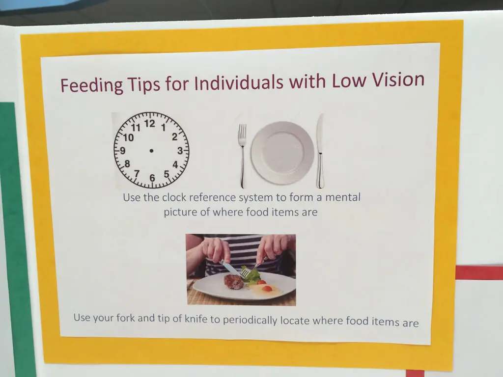 A sign about feeing tips for individuals with low vision, including using clock reference systems to form a mental picture of where food items are and using utensils to locate food items