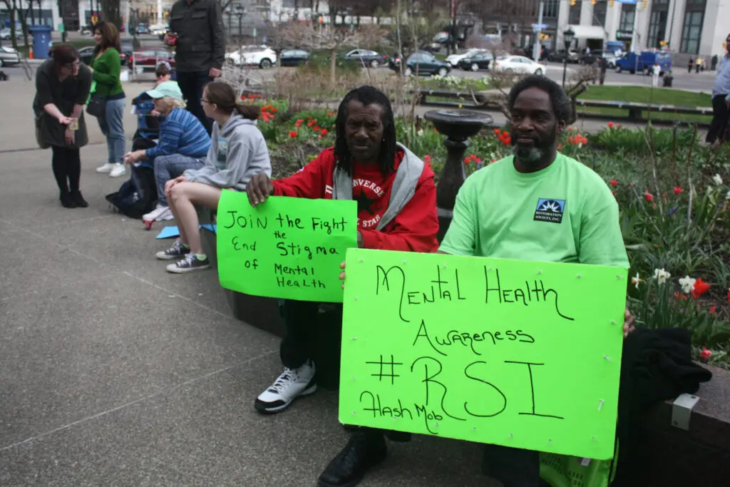 MHPC flash mob attendees with bright green signs for mental health awareness sitting near garden