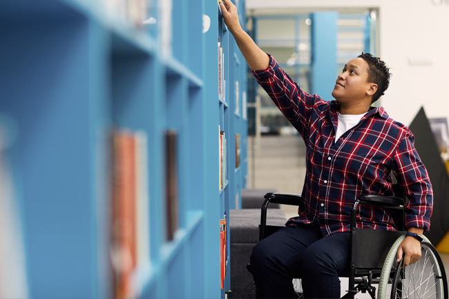Women in wheelchair reaching for book on shelf